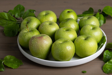 Top view of a composition of fresh ripe green apples and apple tree leaves on a gray background. Selective focus.