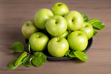 Top view of a composition of fresh ripe green apples and apple tree leaves on a plate wooden background. Selective focus.