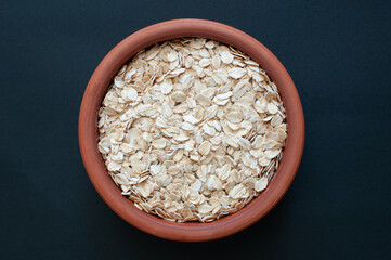 Top view of organic and vegan oat flakes in earthenware casserole. Popular healthy oat meal isolated on dark background.