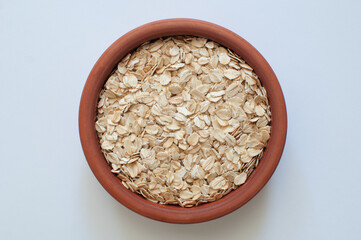 Top view of natural and raw oat flakes in brown earthenware casserole. Popular healthy oat meal isolated on white background.