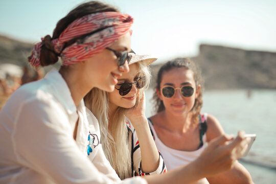three girls on the beach look at pictures through a smartphone