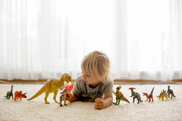 Blond toddler child, playing with dinosaurs at home