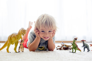 Blond toddler child, playing with dinosaurs at home