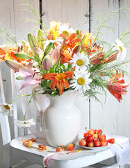 Bouquet in a white ceramic jug and cherries on a white, wooden background