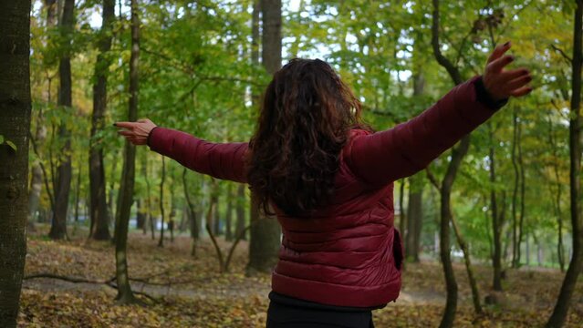 Portrait of happy mature woman stretching hands spinning looking up standing in autumn forest. Excited Caucasian retiree having fun enjoying leisure outdoors in park. Happiness and aging concept