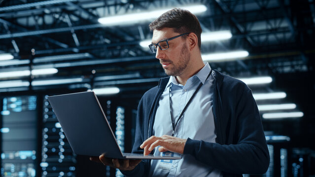 Successful Data Center IT Specialist Using Laptop Computer. Server Farm Cloud Computing Facility with System Administrator Working. Data Protection Engineering Network for Cyber Security.