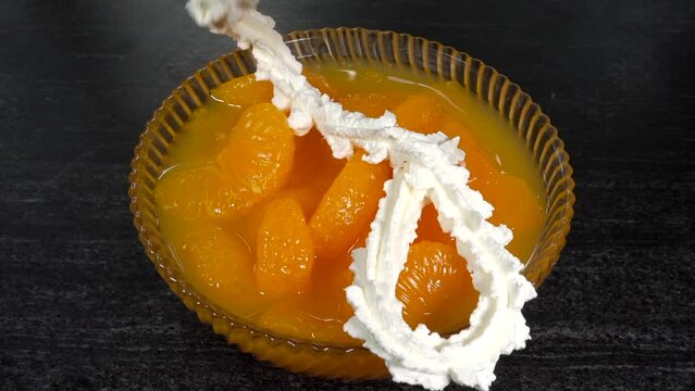 Closeup overhead shot of dairy spray whipping cream being squirted onto mandarin orange segments with juice in a bowl.