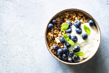 Greek Yogurt with granola and fresh blueberries at light stone table. Top view with copy space.