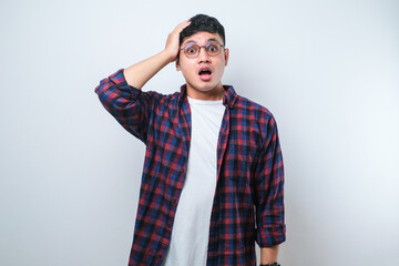 Fototapeta premium Handsome young Asian man wearing casual shirt and glasses standing with a shocked expression and holding his head