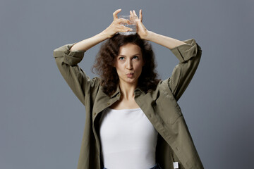 Naklejka premium Funny pretty curly beautiful woman in casual khaki green shirt hold glass of water overhead posing isolated on over gray blue background. Healthy lifestyle. Water is Life concept. Copy space