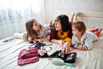 Mother and daughters doing makeup on the bed in the bedroom.