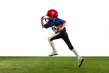 Dynamic portrait of little boy, beginner player of american football training isolated on white background with green grass flooring. Concept of sport, movement, achievements.