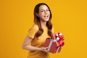 Happy pretty young woman holding gift box on yellow background, blank copy space for your advertising content.