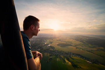 Man enjoying view from hot air balloon during flight over beautiful landscape at sunset. Themes adventure, freedom and travel.. - Powered by Adobe