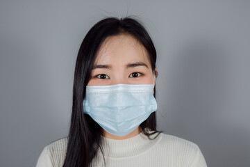 Asian woman wearing a medical face mask to protect Covid-19 (Coronavirus) on gray background