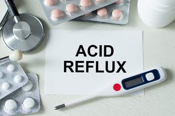 ACID REFLUX text on a card on a table next to a thermometer, tablets and stethoscope