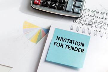 INVITATION FOR TENDER text inscription on a blue card on the background of a notebook on the table