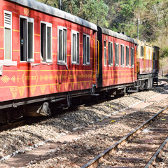 Fototapeta premium Toy Train moving on mountain slopes, beautiful view, one side mountain, one side valley moving on railway to the hill, among green natural forest. Toy train from Kalka to Shimla in India