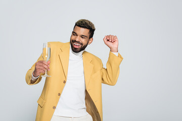 joyful african american man in stylish outfit holding glass of champagne isolated on grey. © LIGHTFIELD STUDIOS