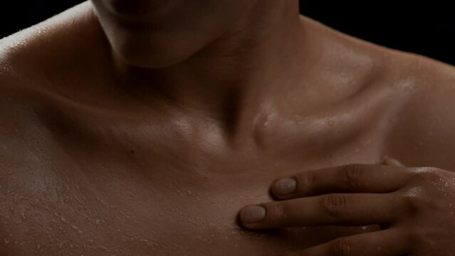 Big close-up shot of young good-looking slim African American woman strokes her wet clavicles on black background | Body care concept