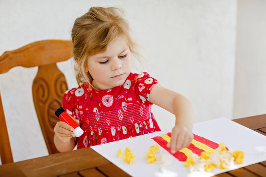 Little creative toddler girl painting with finger colors popcorn box and making paper corns with glue. Active child having fun with drawing doing handicraft. Education for kids. Creaitve activity.