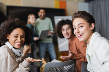 happy multiethnic students looking at camera near classmates on blurred background.