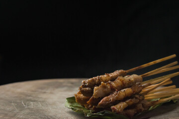 front view of grilled skewered pork(Moo Ping) placed on the banana leaves and wood floor, black background
