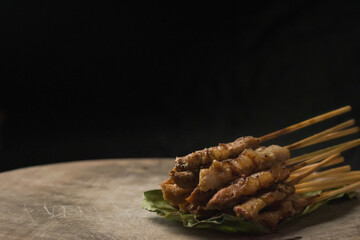 front view of grilled skewered pork(Moo Ping) placed on the banana leaves and wood floor, black background