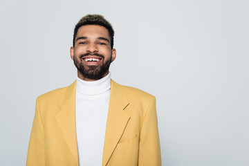 portrait of happy african american man with blue eyes in stylish outfit isolated on grey.