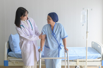 Doctor helping cancer patient woman wearing head scarf with walker at hospital, health care and medical concept..