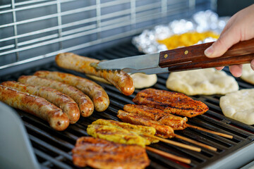 Assorted meat grilling over the hot fire on a portable barbecue with steak, sausage, kebabs, chicken , spare ribs and corn and bread. man grills food