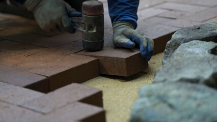 Closeup of a man setting brick pavers into place in a herringbone pattern in hardscaping landscaping patio project.