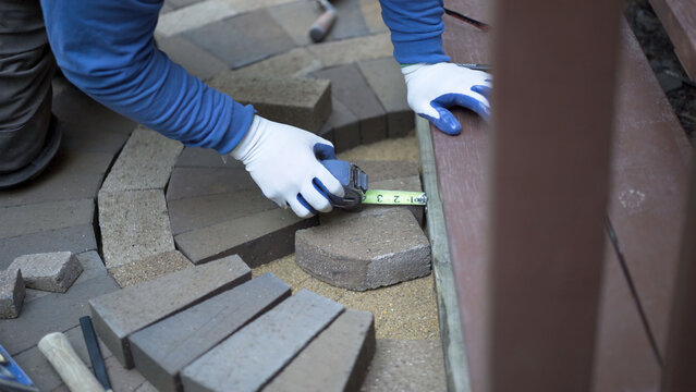 Man measuring and marking bricks for a decorative two tone paver pattern in front a stairway.