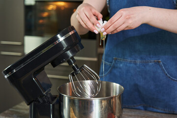 a woman's hand breaks a chicken egg into a large culinary mixer