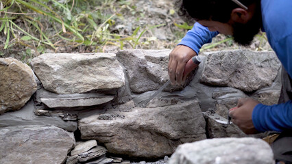 Closeup of putting mortar between large stones in a rock wall design in hardscaping landscaping project.