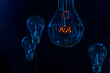Glowing lamp, tungsten light bulb lit on black background,  close up shot, on wood table,  idea...