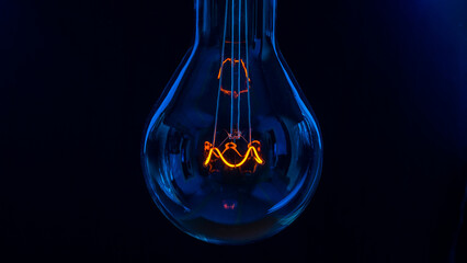 Glowing lamp, tungsten light bulb lit on black background,  close up shot, on wood table,  idea...