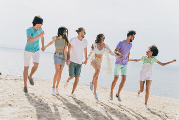 Full size photo of carefree overjoyed people hold arms running have fun chilling sand beach outdoors