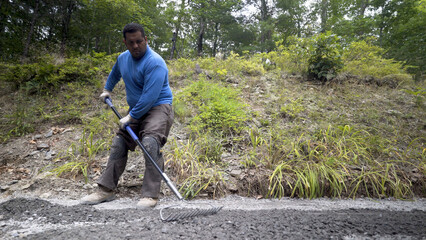 Laborer pushing excess gravel off of the area to be hardscaped.