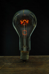 Glowing lamp, tungsten light bulb lit on black background,  close up shot, on wood table,  idea...