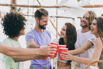 Portrait of cheerful carefree buddies hold plastic bear cups say toasts clink hang out outdoors
