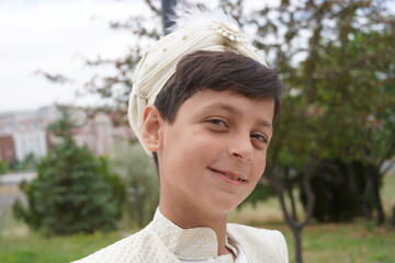 Turkish boy wearing traditional clothing during a circumcision ceremony. Boy standing outdoors among trees.