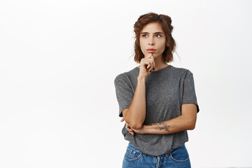 Woman with thoughtful face touching chin, thinking, making decision, standing in grey tshirt over white background