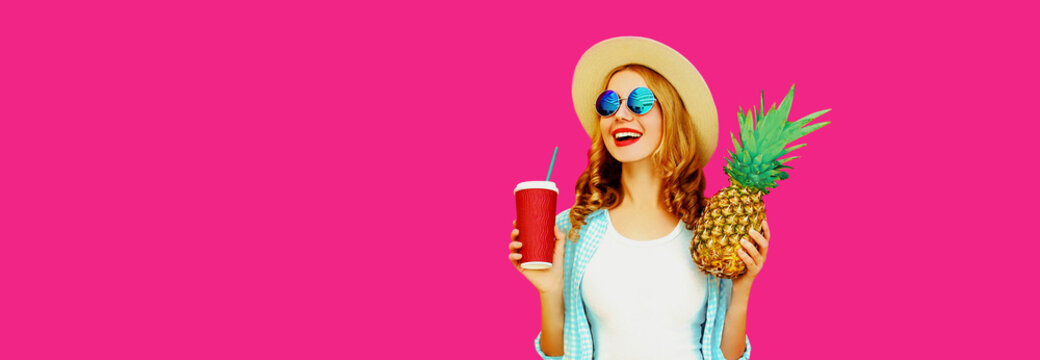 Summer portrait of happy smiling woman looking away with cup of juice and pineapple wearing straw hat, sunglasses on pink background, blank copy space for advertising text