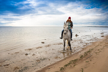 wearing jacket, jeans and warm hat horsewoman takes a gray hackney along waterside