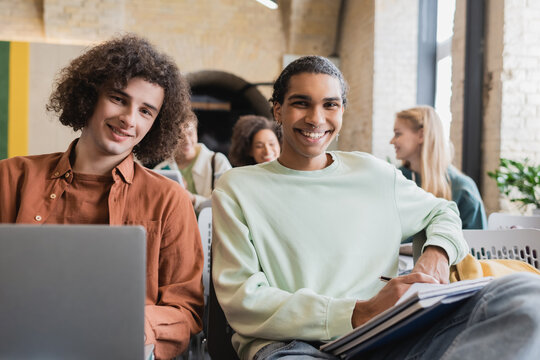 happy african american student and his friend with laptop looking at camera during lecture.
