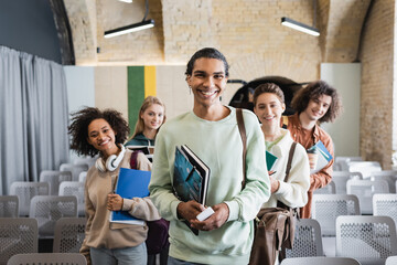 happy african american man looking at camera together with multiethnic friends in auditorium.