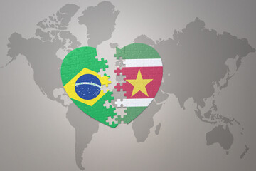 puzzle heart with the national flag of brazil and suriname on a world map background.Concept.