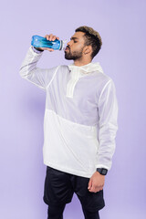 young african american sportsman holding sports bottle and drinking refreshing water on purple.