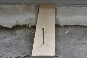 A self-tapping screw twisted into a wooden block on a defocused background of repair work
